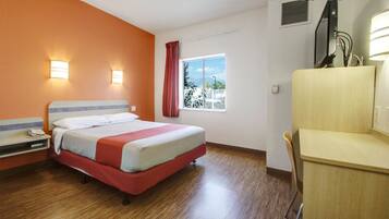 Quarto de hotel com cama, escrivaninha, cadeira, janela com vista e televisão.