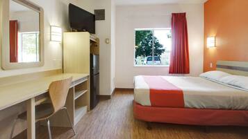 Habitación de hotel con cama, escritorio con silla, televisión, ventana con cortinas y vistas al exterior.