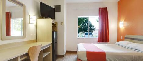 Camera d'albergo con un letto, una scrivania con una sedia, un televisore, una finestra con tende e vista sull'esterno.