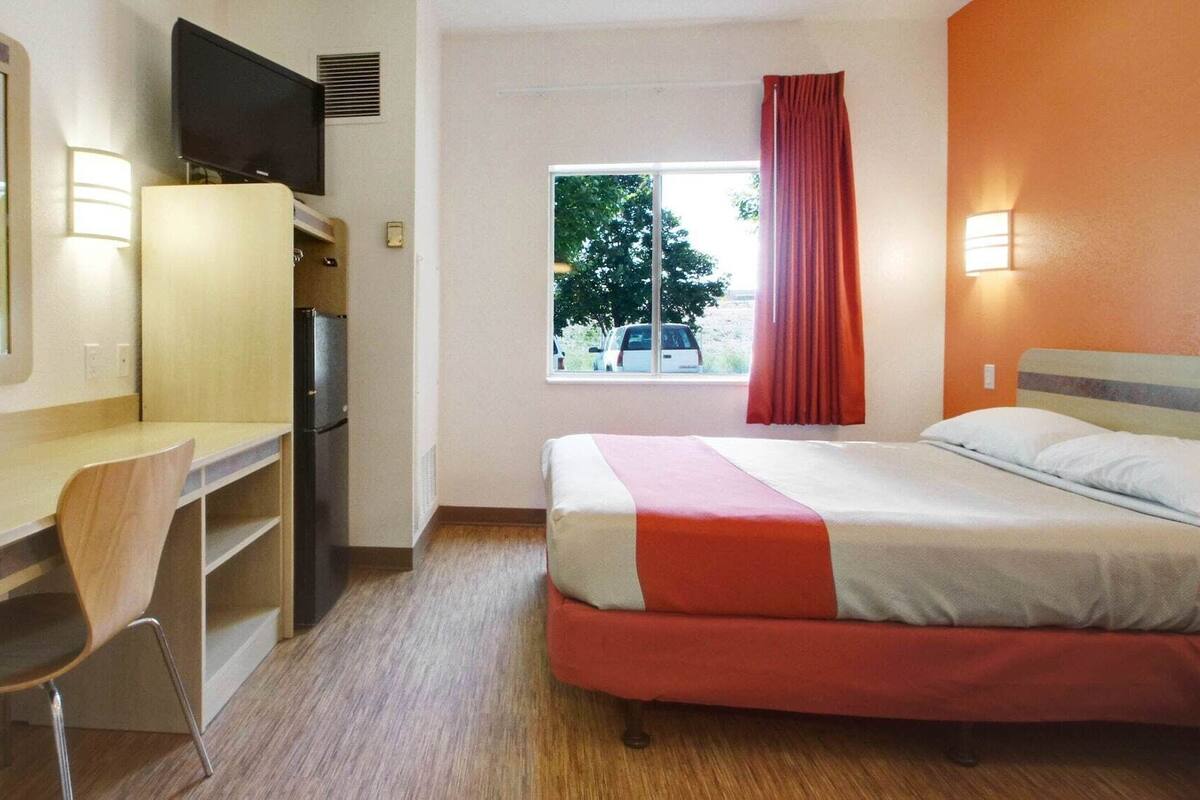 Ein Hotelzimmer mit Bett, Schreibtisch mit Stuhl, Fernseher, einem Fenster mit Vorhängen und Blick nach draußen.