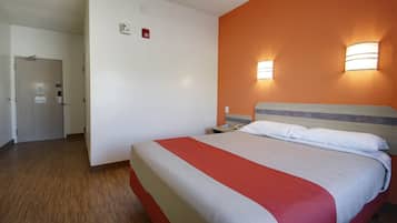 A hotel room with a bed, a nightstand, a wall-mounted lamp, and a door.