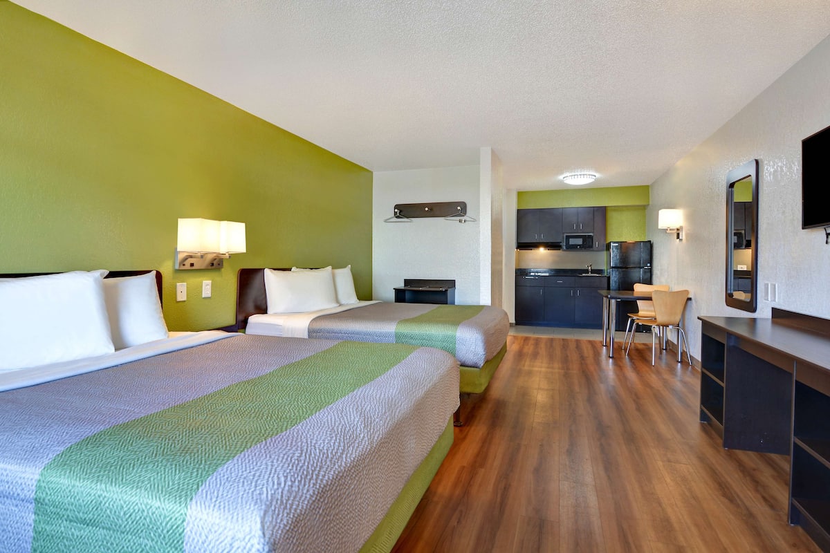 A hotel room with two beds, a kitchenette, and a dining area.
