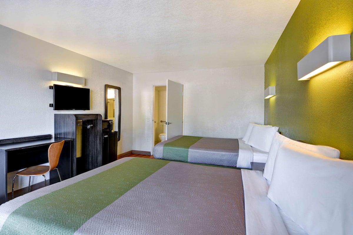 A hotel room with a large bed, a desk with a chair, a television mounted on the wall, and a bathroom door.