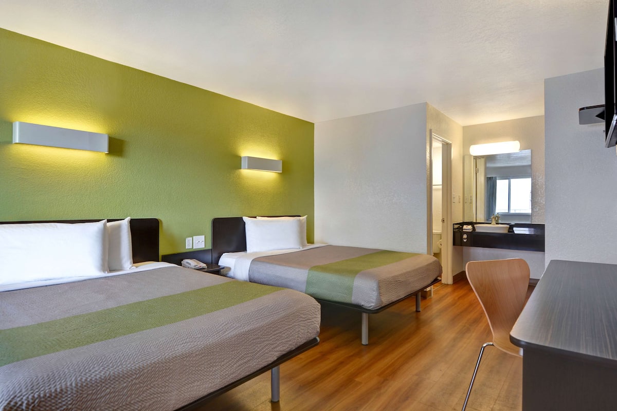 A hotel room with two beds, a desk, a chair, and a bathroom visible through an open door.