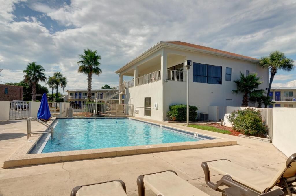 A swimming pool with lounge chairs, a covered area, and palm trees.