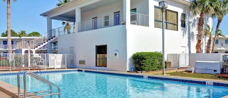 A two-story hotel with a swimming pool, a balcony, and palm trees.