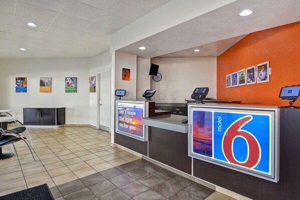 A motel reception desk with a digital display, a clock, and a series of framed pictures on the wall. - Motel 6 Destin, FL (Destin)