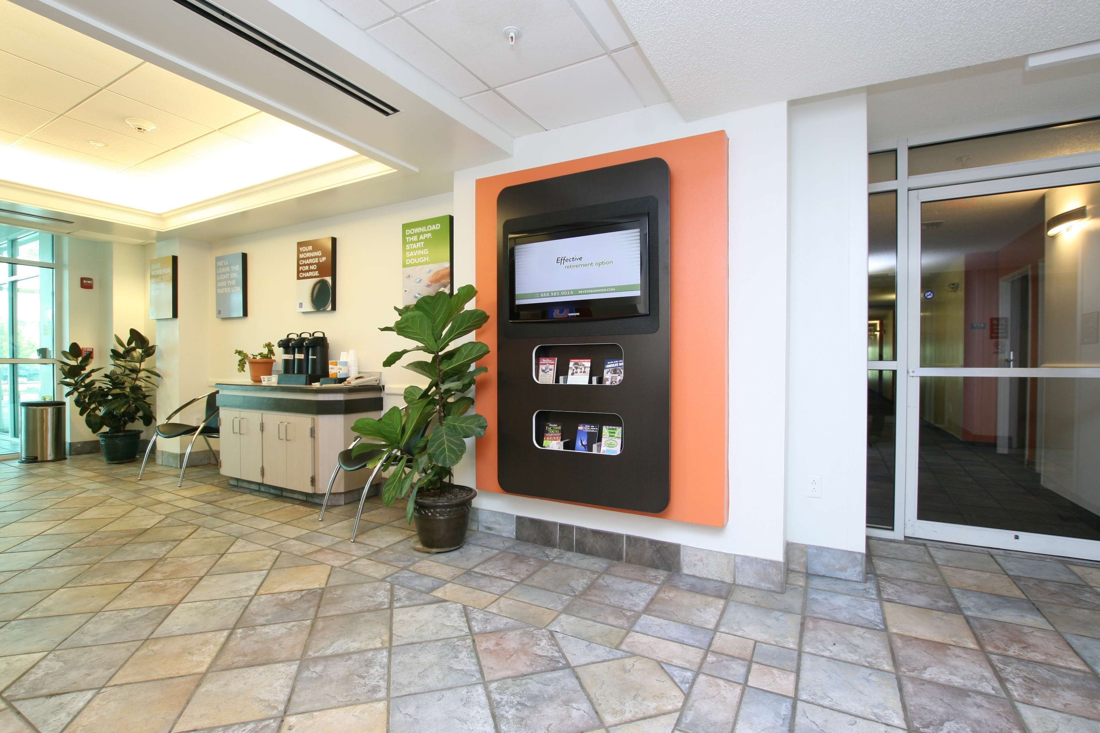 A reception area with a digital kiosk, potted plants, and a tiled floor.