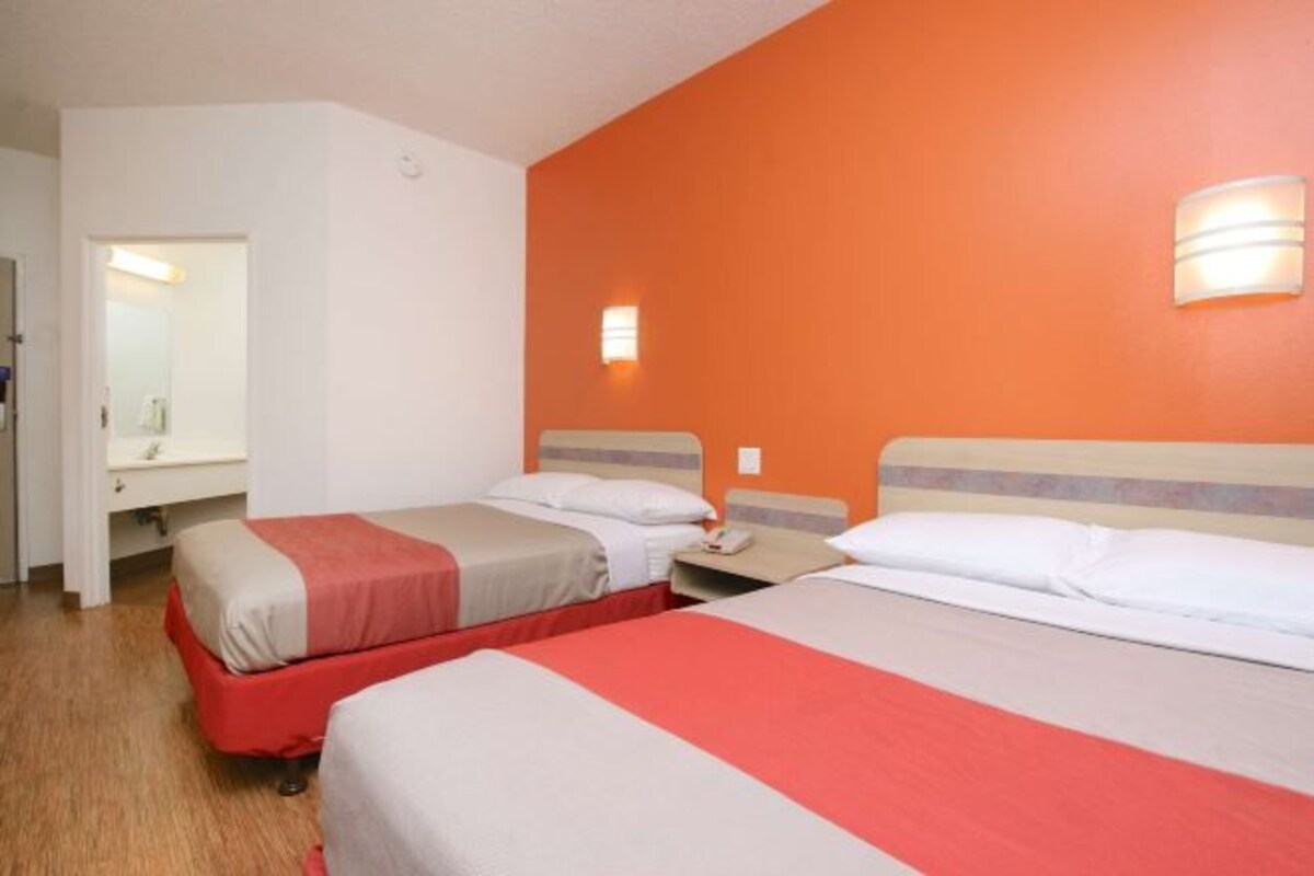 A hotel room with two beds, a white sink, and an orange accent wall.