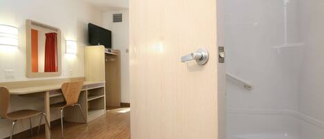 Camera d'albergo con una scrivania in legno, due sedie, televisione, uno specchio e zona doccia.