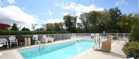 Una piscina con sillones de descanso y un área cercada.