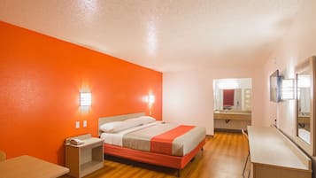 Quarto de hotel com cama, mesa de cabeceira e espelho.