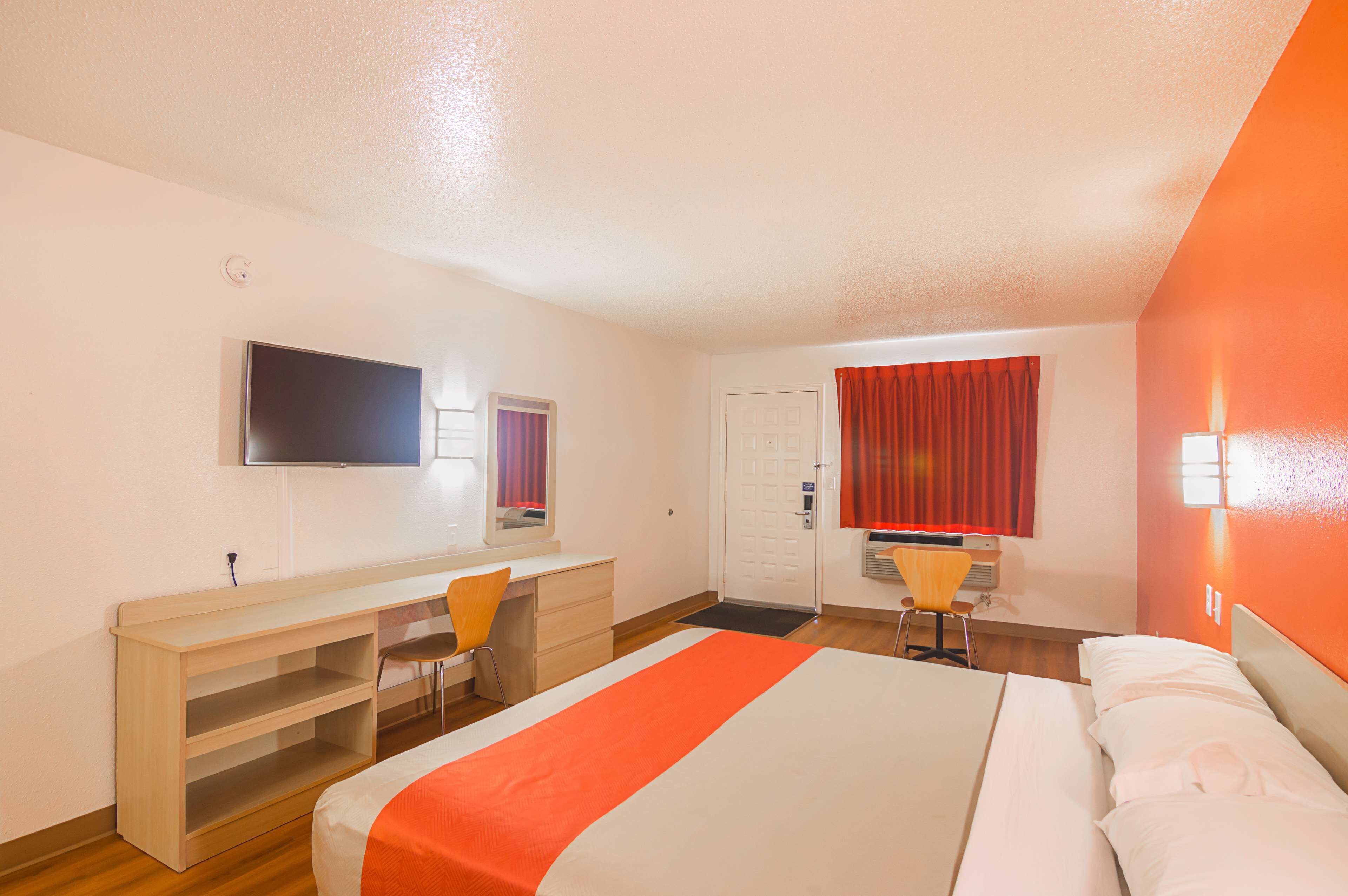 Habitación de hotel con cama, escritorio, silla, televisor y puerta.