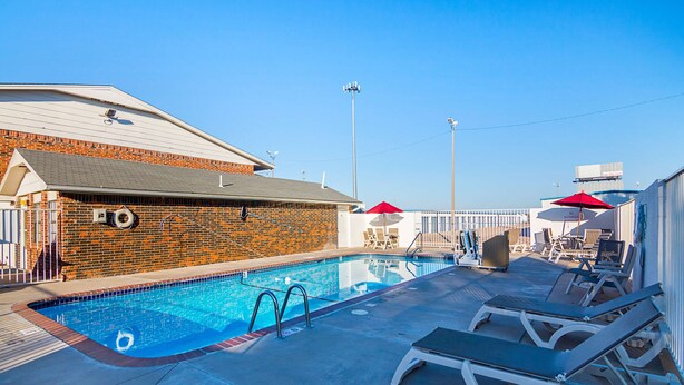 A swimming pool with lounge chairs and umbrellas, surrounded by a brick building and a clear sky. - Motel 6 Lawton, OK (Lawton)