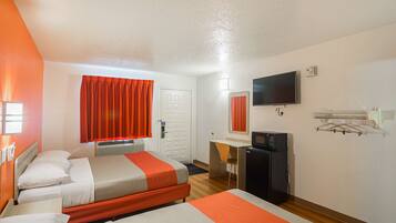 A hotel room with two beds, a desk, a television, and a refrigerator.