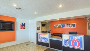 A hotel reception area with a modern design, featuring a reception desk, a digital display, and a wall-mounted television. - Motel 6 Lawton, OK (Lawton)
