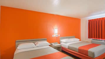 A hotel room with two beds, orange walls, a nightstand with a phone, and a window with red curtains.