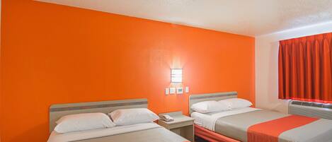 A hotel room with two beds, orange walls, a nightstand with a phone, and a window with red curtains.