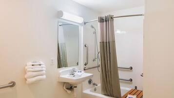 A bathroom with a sink, mirror, shower, and towel rack.
