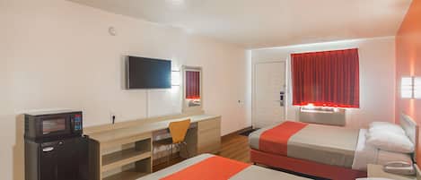 Habitación de hotel con dos camas, un escritorio con silla, microondas, televisor y ventana con cortinas rojas.