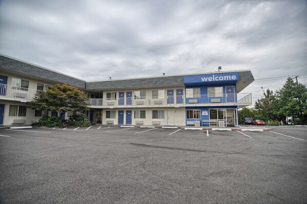 A motel with a 'Welcome' sign, multiple rooms, a parking lot, and a small garden area. - Motel 6 Coeur D'Alene, ID (Coeur d'Alene)