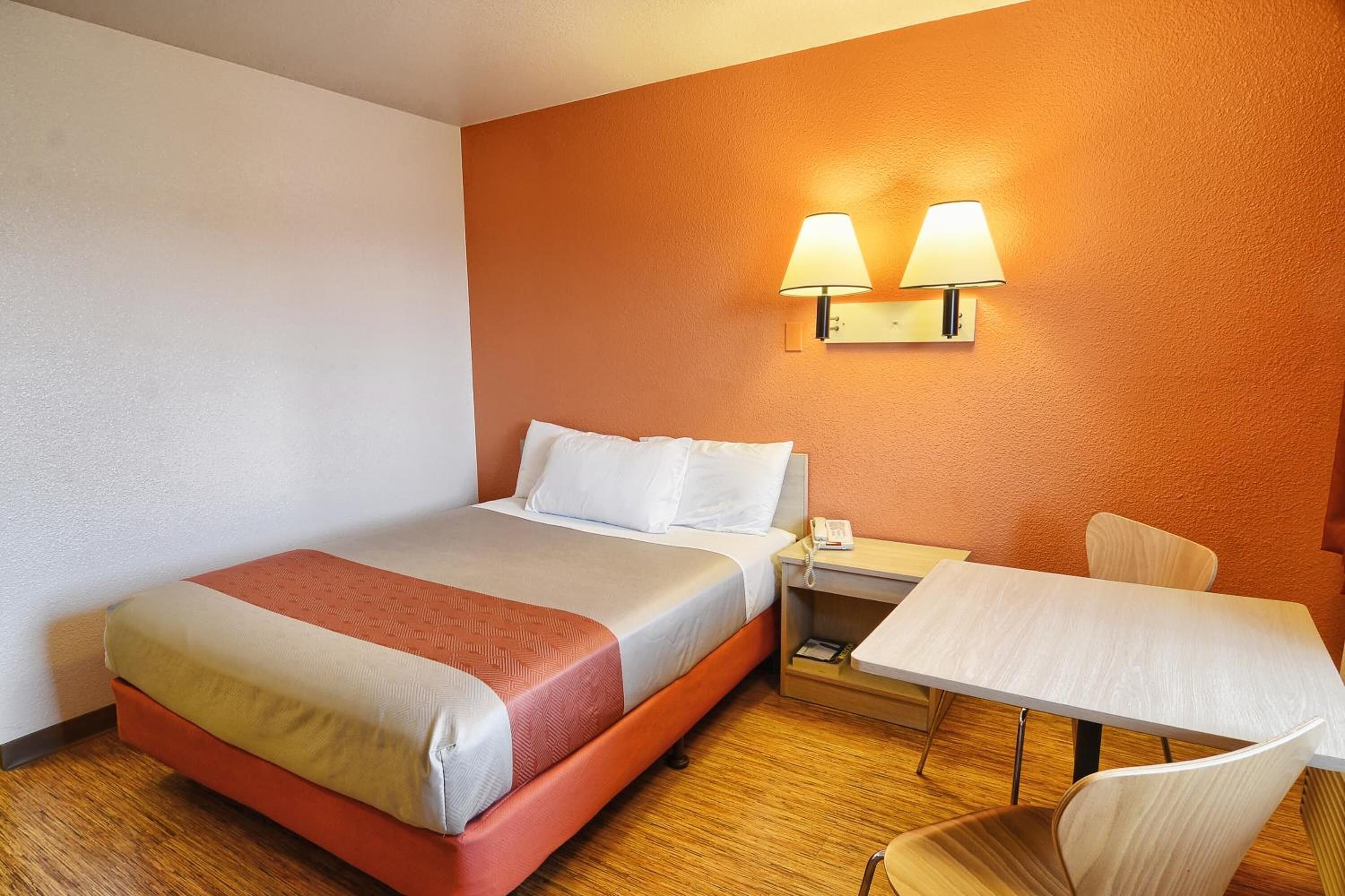 A hotel room with a bed, bedside table, lamp, and a small table with a chair.