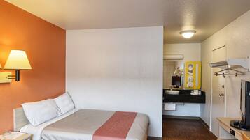 A hotel room with a bed, a nightstand, a lamp, a bathroom with a mirror, sink, and towel rack.