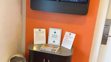 A reception area with a TV mounted on the wall displaying a show, a cabinet with informational pamphlets, and a trash bin.