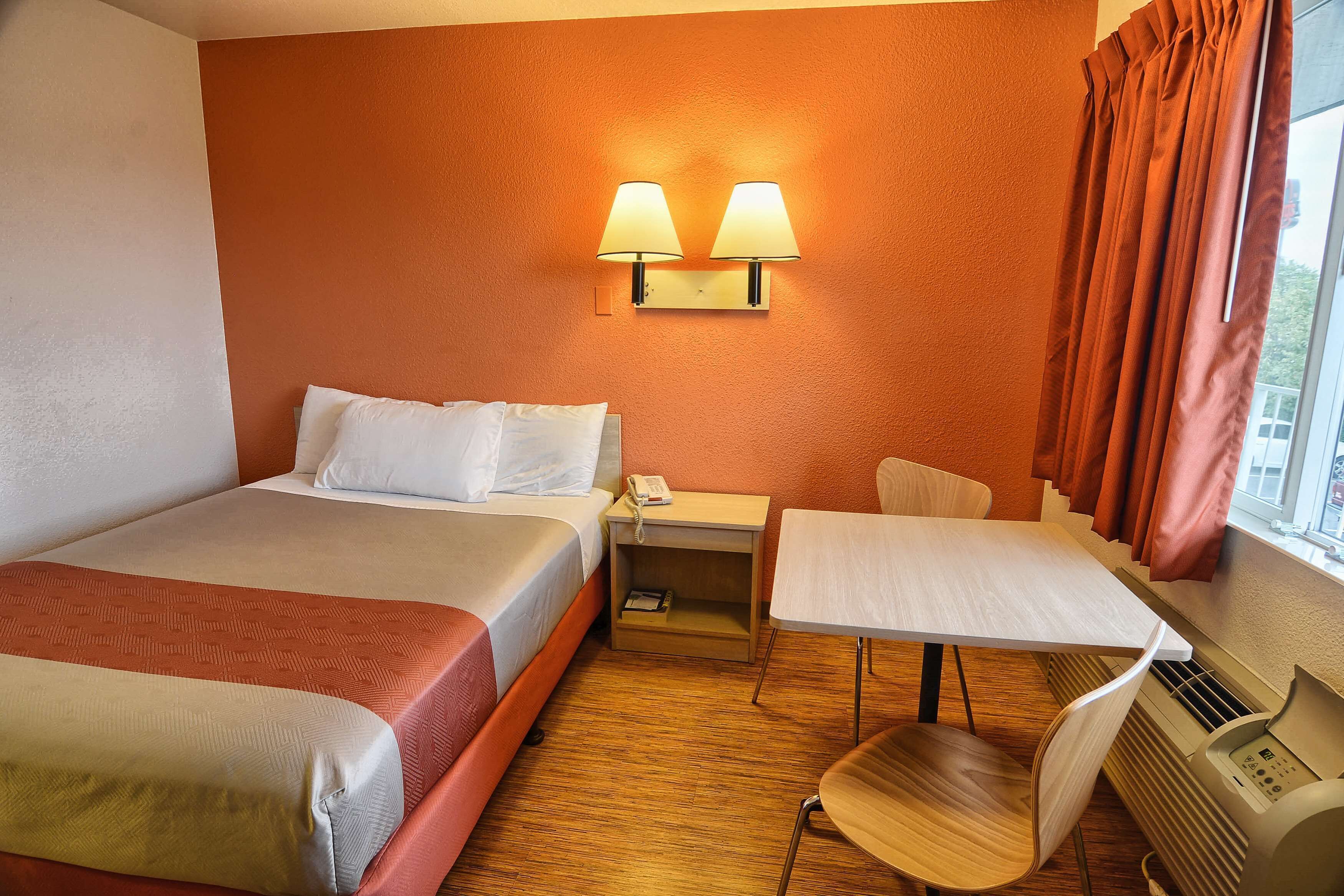 A hotel room with a bed, a desk, a chair, and a window with curtains.