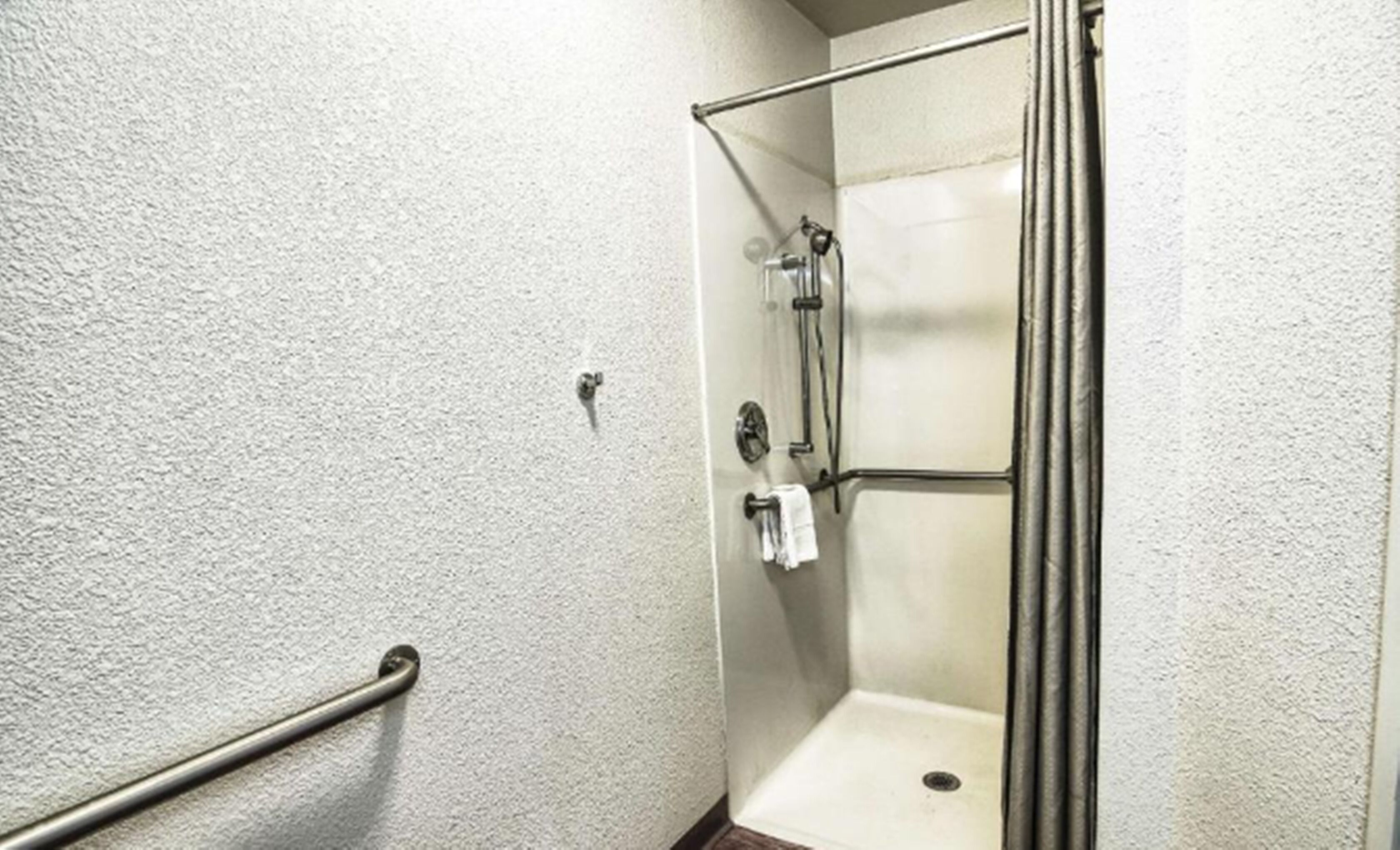 A shower with a glass door, a towel rack, and a handrail.