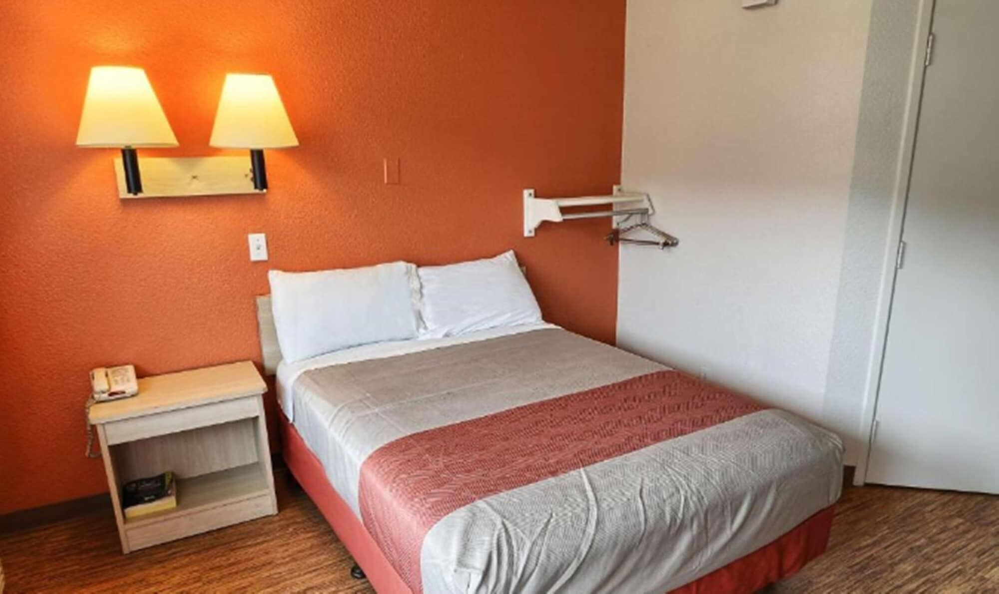 A hotel room with a bed, two bedside lamps, a nightstand, and a wardrobe.