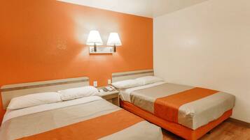 A hotel room with two beds, each with white and orange bedding, a nightstand with a phone and lamp, and an orange accent wall with two wall-mounted lamps.