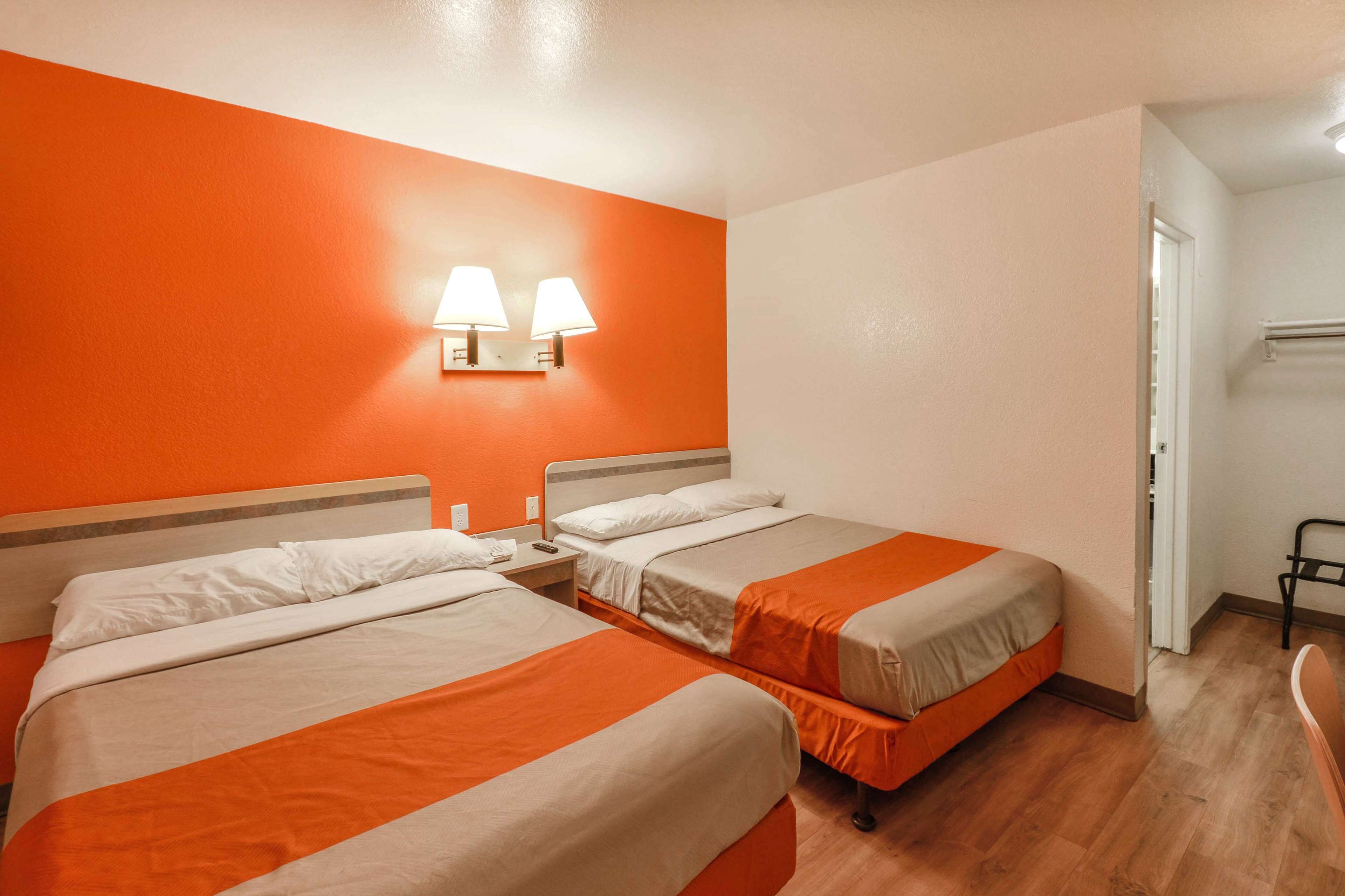 A hotel room with two beds, a nightstand, and a wall-mounted lamp.