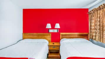 Een hotelkamer met twee bedden, een rode accentmuur, een nachtkastje met lampen en kamergordijnen met een patroon.