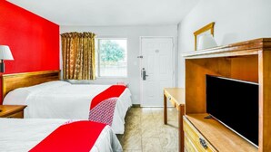 A hotel room with two beds, a TV, a desk, and a window with curtains.