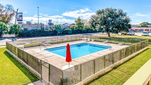 A rectangular swimming pool with a red umbrella, surrounded by a metal fence and a grassy area.