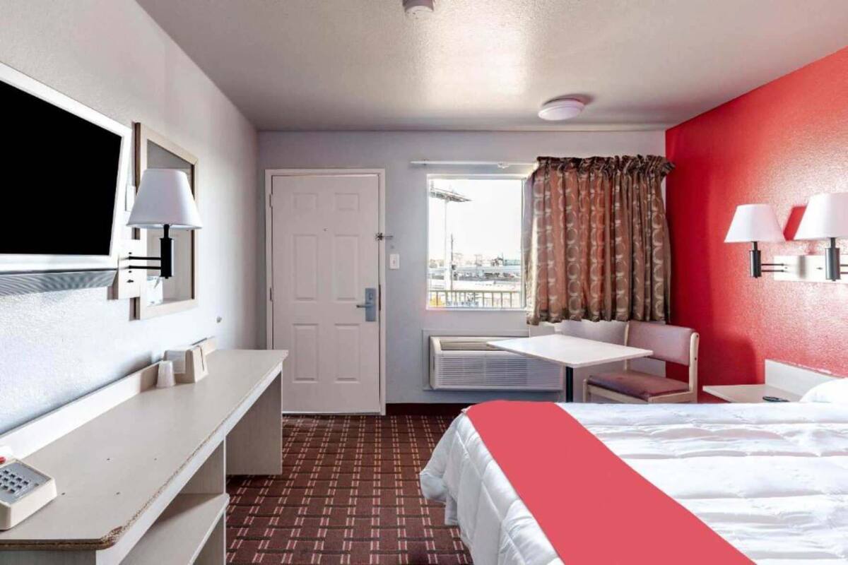 Une chambre d’hôtel équipée d’un lit, d’un bureau, d’une chaise, d’une télévision et d’une fenêtre avec des rideaux, offrant une vue sur l’extérieur.