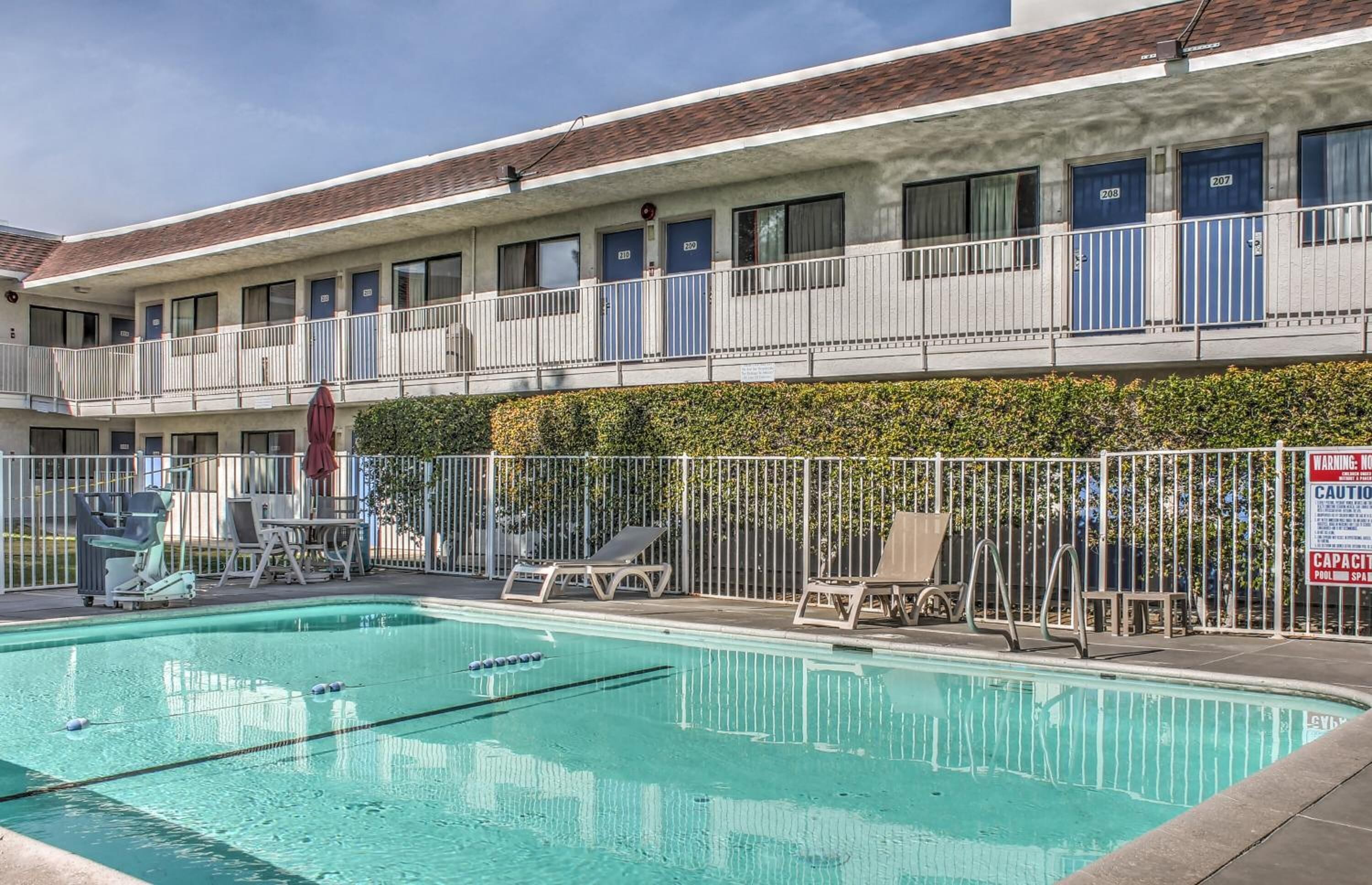 A motel with a swimming pool, multiple balconies, and a fenced area with lounge chairs.