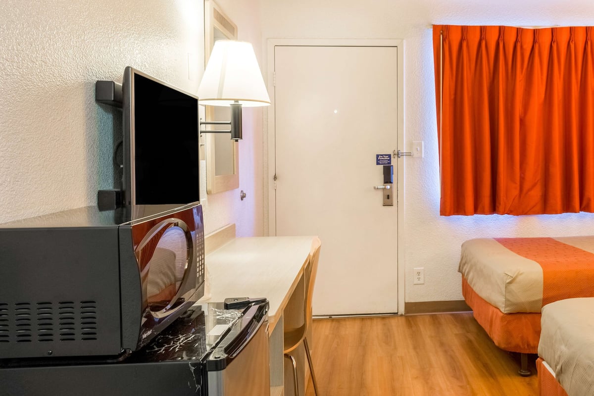 A hotel room with a bed, a desk with a television, a lamp, and a door.