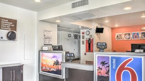 A motel reception area with a counter, a clock, a TV, and a sign indicating the motel number. - Motel 6 Mojave, CA (Mojave)