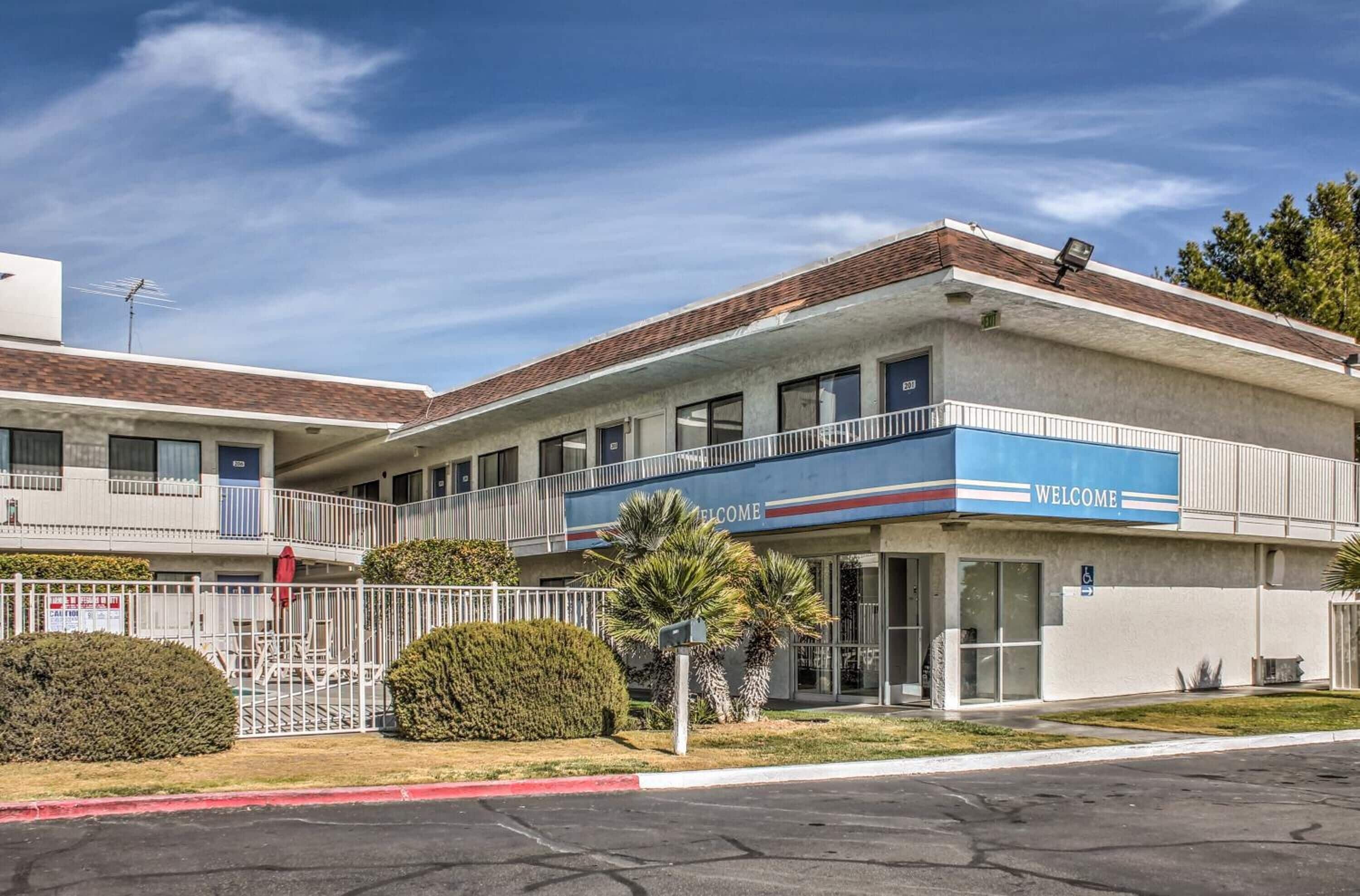 A two-story motel with a 'WELCOME' sign, a covered parking area, and a small garden with palm trees.