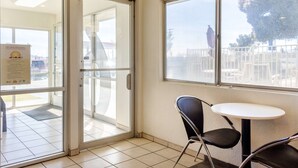 A hotel lobby with a glass door entrance, a small round table, and a chair. - Motel 6 Mojave, CA (Mojave)