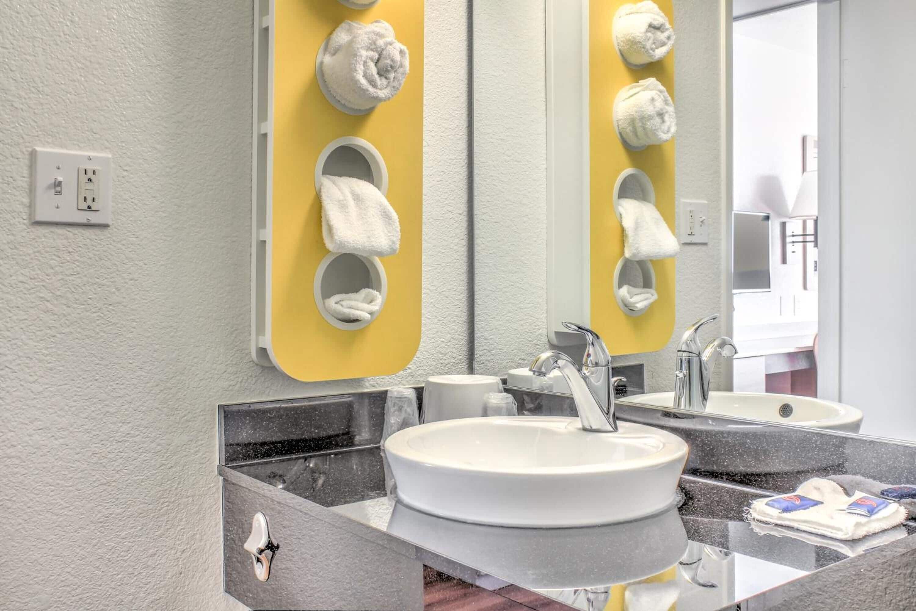 Une salle de bain moderne avec un lavabo blanc, deux miroirs et un porte-serviettes jaune.