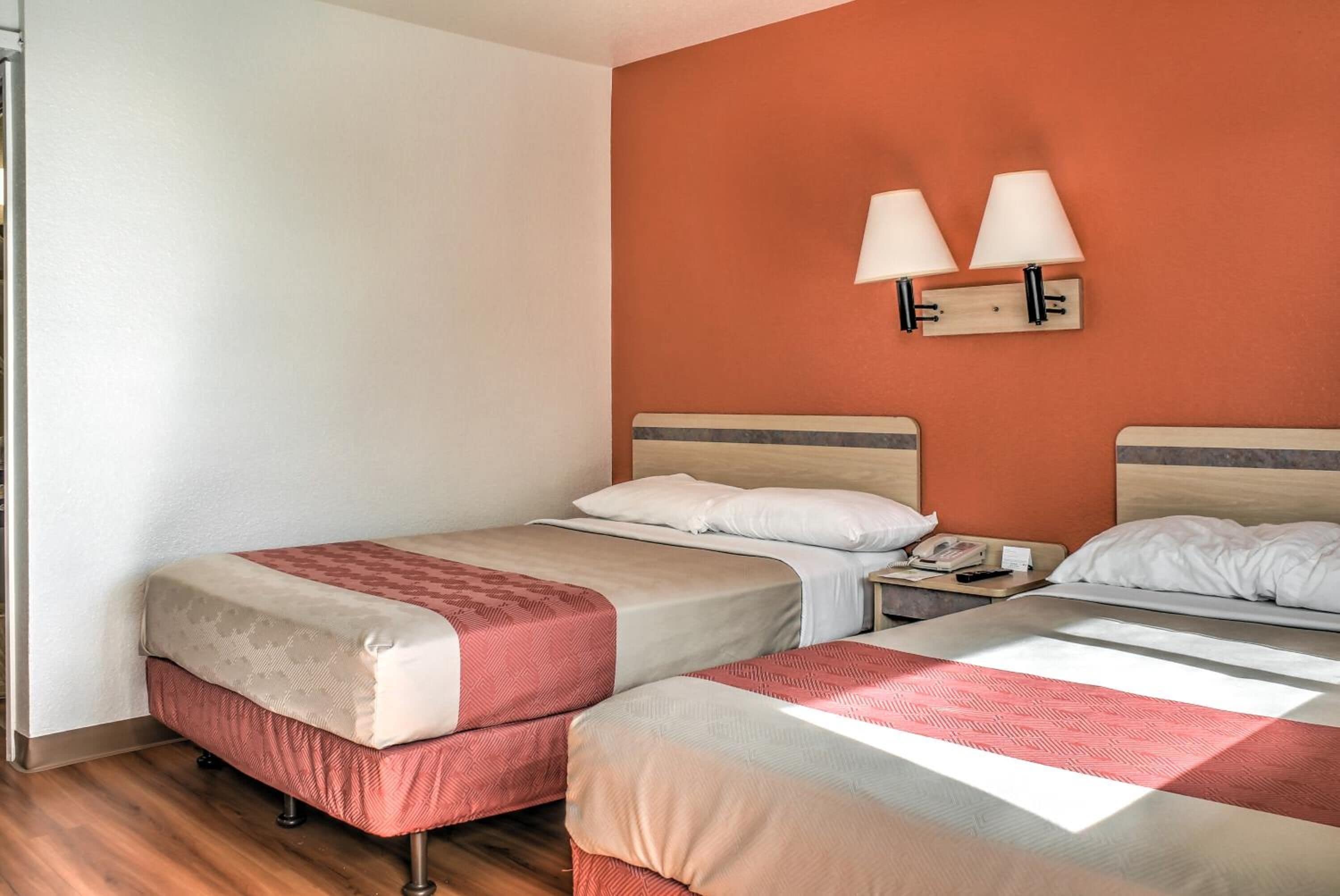 A hotel room with two beds, a nightstand, and a lamp.