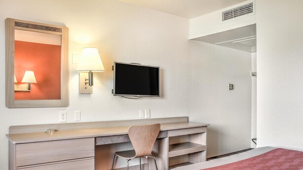 A hotel room with a bed, a desk with a chair, a television, a mirror, and a wall-mounted lamp. - Motel 6 Mojave, CA (Mojave)