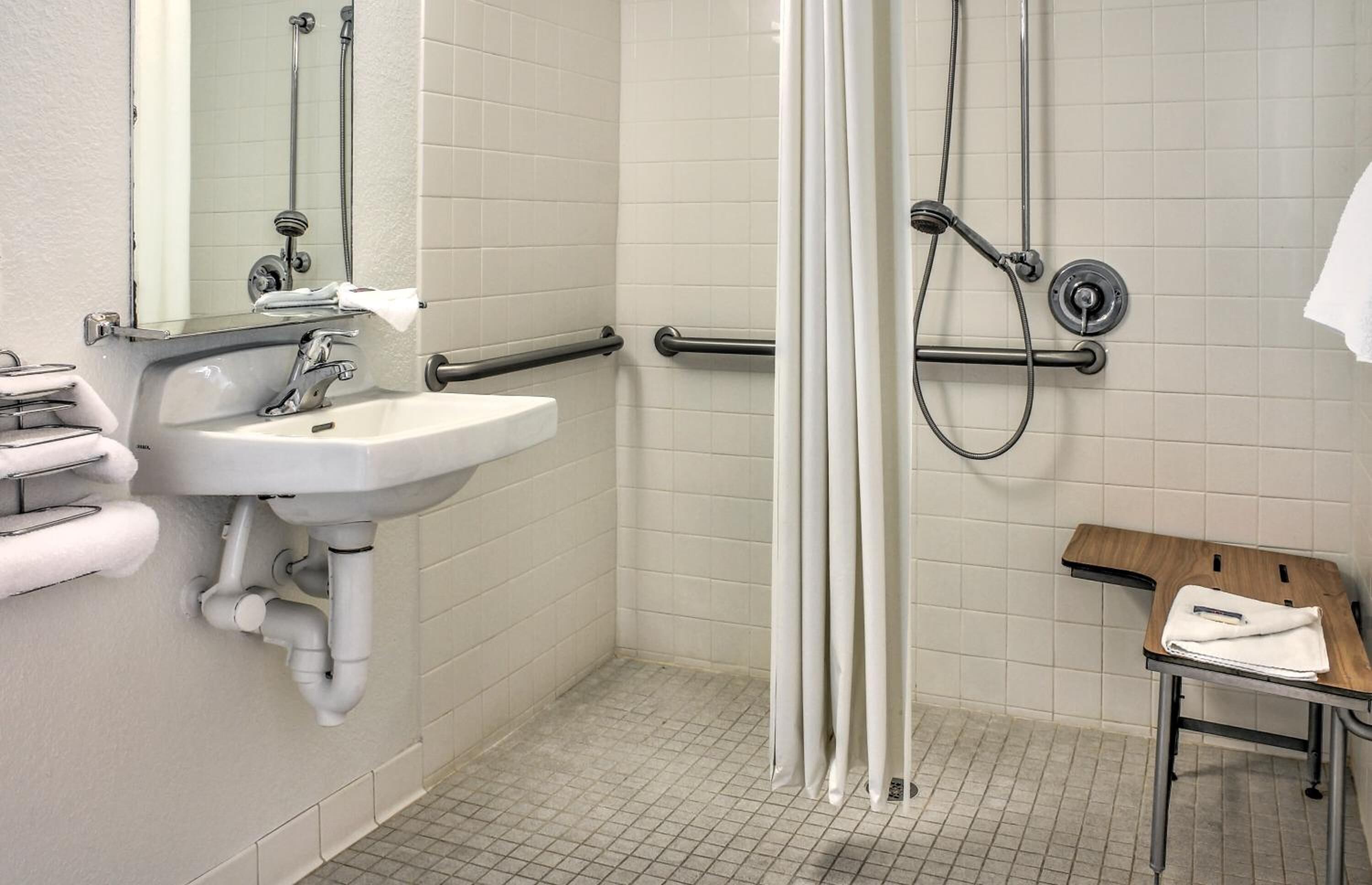A bathroom with a sink, mirror, shower, and a bench.