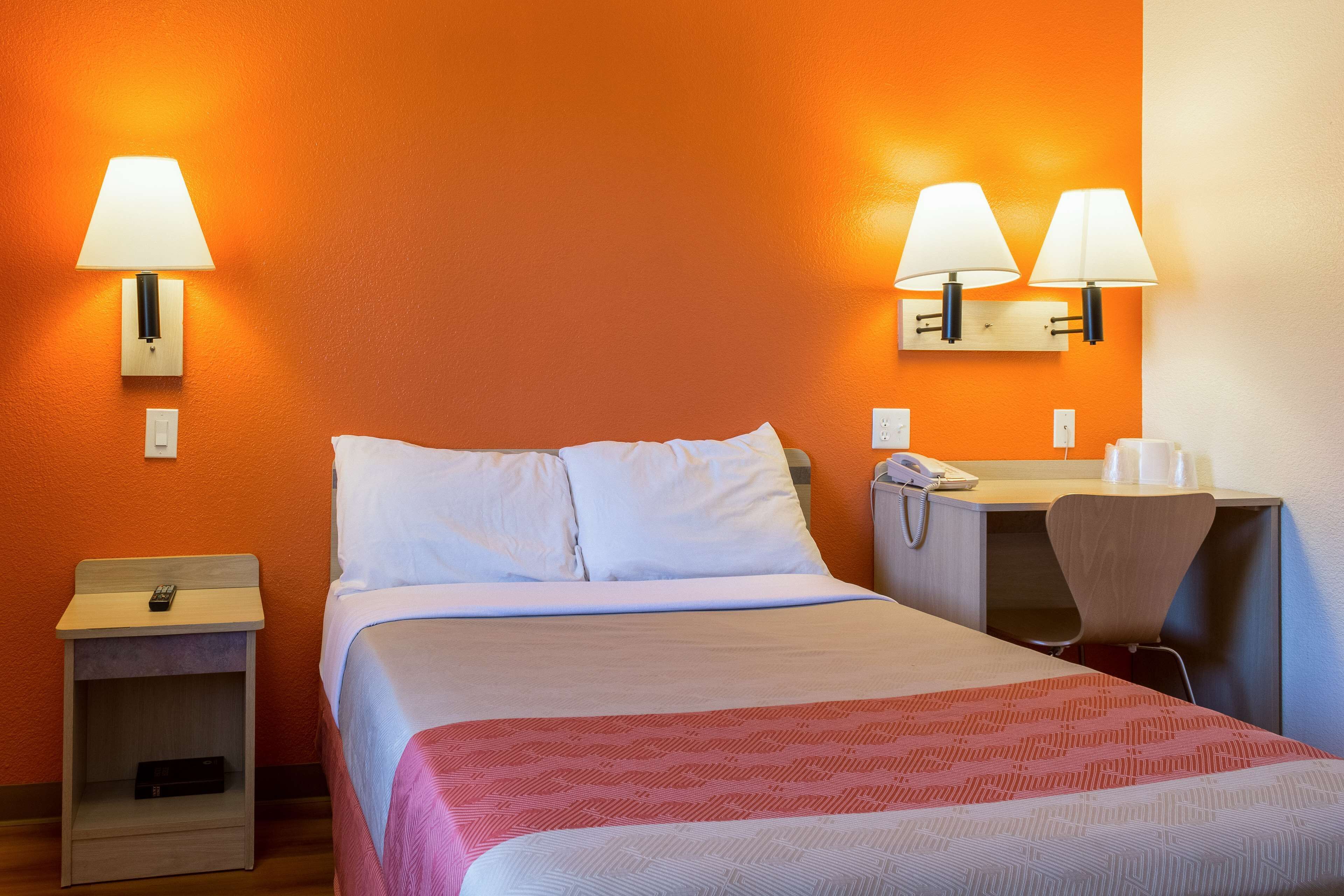 Una habitación de hotel con una cama, mesitas de noche, un escritorio y dos lámparas de pared.