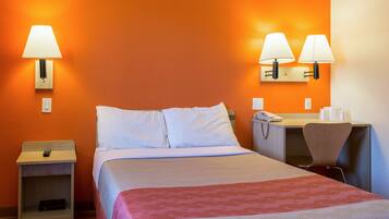Una habitación de hotel con una cama, mesitas de noche, un escritorio y dos lámparas de pared.