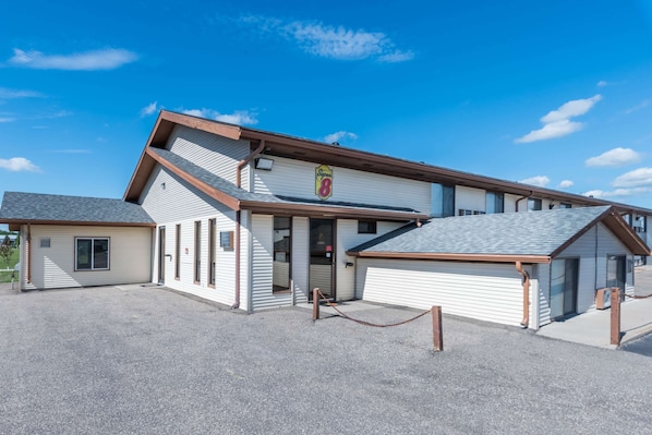 A two-story building with a sloped roof, a prominent sign with the number 8, and a gravel driveway. - Super 8 by Wyndham Devils Lake (Devils Lake)