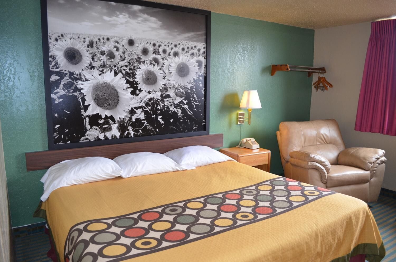 A hotel room with a large bed, a chair, a nightstand with a lamp, and a wall-mounted telephone.